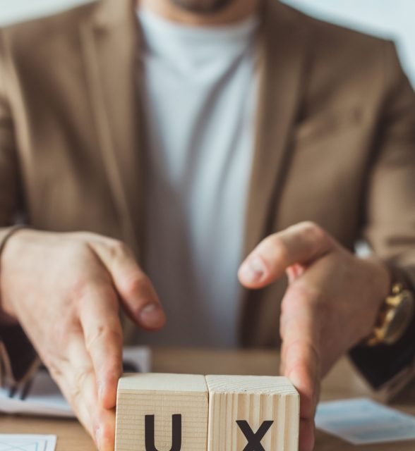 Cropped view of designer holding cubes with ux letters at table with sketches